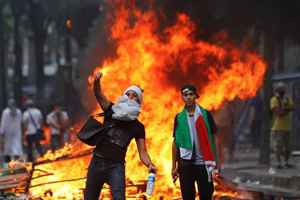 Pro-Palestinian demonstrator throws a stone towards riot police, during a demonstration in Paris, Saturday, July 19, 2014. Police have clashed with thousands of pro-Palestinian protesters who defied a ban in Paris on marching to protest the Israeli offensive in Gaza. Some of the protesters threw stones and other objects at riot police, who responded with rounds of tear gas.