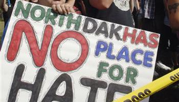 In this Sept. 22, 2013. file photo, Jay Schechter holds a sign, while participating in a protest rally outside Craig Cobb's house in Leith, N.D. The town of Leith has invited Gov. Jack Dalrymple and members of North Dakota's congressional delegation to help the community celebrate its birthday and the end of a months-long clash with Cobb, who unsuccessfully tried to take over the town. Leith is holding is 105th birthday bash the weekend of July 19-20.