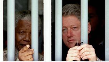 In this March 27, 1998 file photo, South African President Nelson Mandela, left, and U.S. President Bill Clinton peer through the bars of prison cell No. 5, the cramped, gray cell where Mandela was jailed for 18 years in his struggle against apartheid, on Robben Island, South Africa. South Africa's president Jacob Zuma says, Thursday, Dec. 5, 2013, that Mandela has died. He was 95.