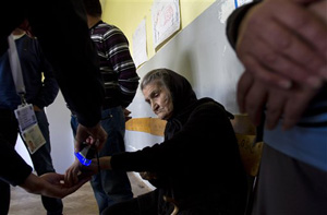 Official checks a old Serb woman for electoral stain before she is allowed to vote at a polling station in Kosovo capital Pristina on Sunday, Nov 3, 2013.