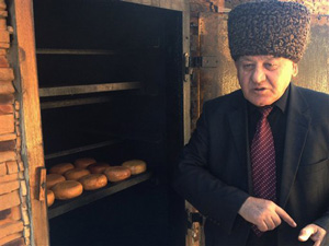 In this photo taken Saturday, Feb. 15, 2014, Aisa Achmizov, director of the local folk art museum, shows off traditional smoked cheese made by his Circassian tribe in the village of Bolshoi Kichmai, Russia. Circassians are a Muslim ethnic group who live in villages sprinkled through the Sochi region, just a few dozen kilometers (miles) from where the Winter Olympic games are being played out in gleaming arenas. Photo Credit: The Associated Press, Angela Charlton.