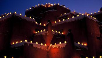 This undated image provided by New Mexico Tourism shows farolitos, which are candles in paper bags, flickering against the night sky atop Santa Fe’s Inn at Loretto. The farolito lanterns, also called luminarias, are a New Mexico holiday tradition.