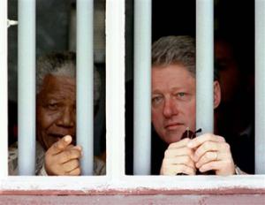 In this March 27, 1998 file photo, South African President Nelson Mandela, left, and U.S. President Bill Clinton peer through the bars of prison cell No. 5, the cramped, gray cell where Mandela was jailed for 18 years in his struggle against apartheid, on Robben Island, South Africa. South Africa's president Jacob Zuma says, Thursday, Dec. 5, 2013, that Mandela has died. He was 95.